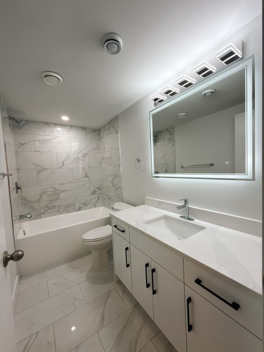 Finished bathroom with marble tile, LED mirror and white vanity