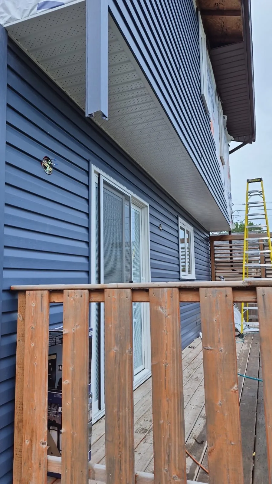 Completed blue vinyl siding with new wood deck railing detail