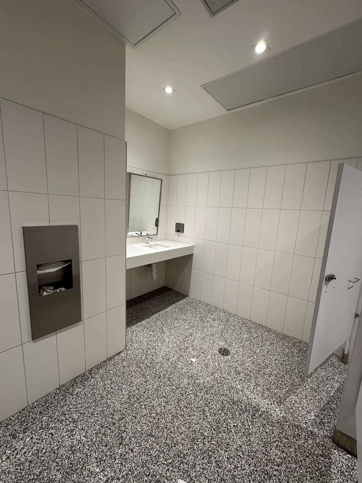 Finished commercial washroom with floating white sink and terrazzo-look floor
