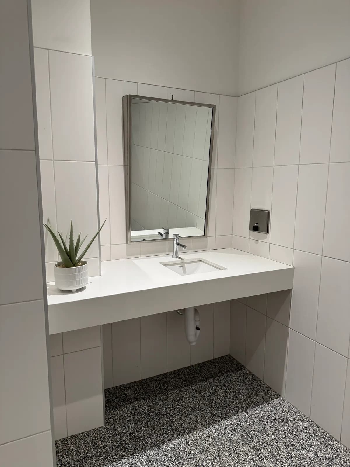 Finished commercial washroom vanity with quartz sink and terrazzo-look floor