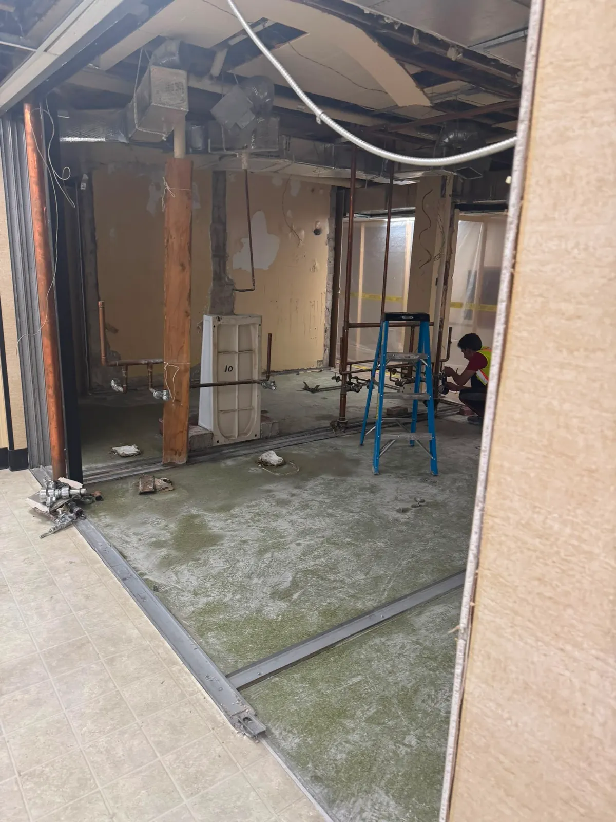 Gutted commercial room with exposed framing and a worker at floor level