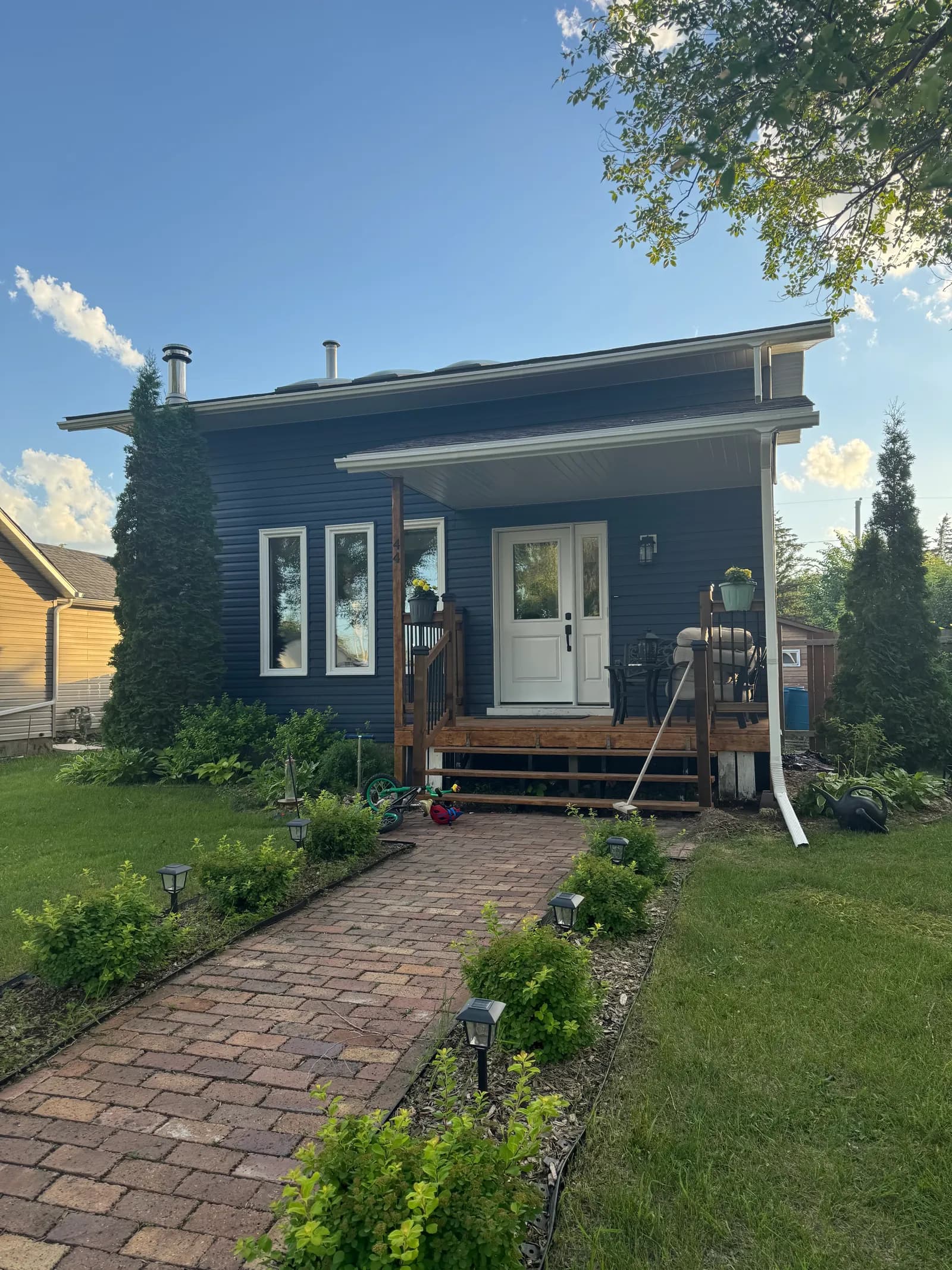 Completed house exterior with new dark blue siding, covered porch, white double door and paver walkway