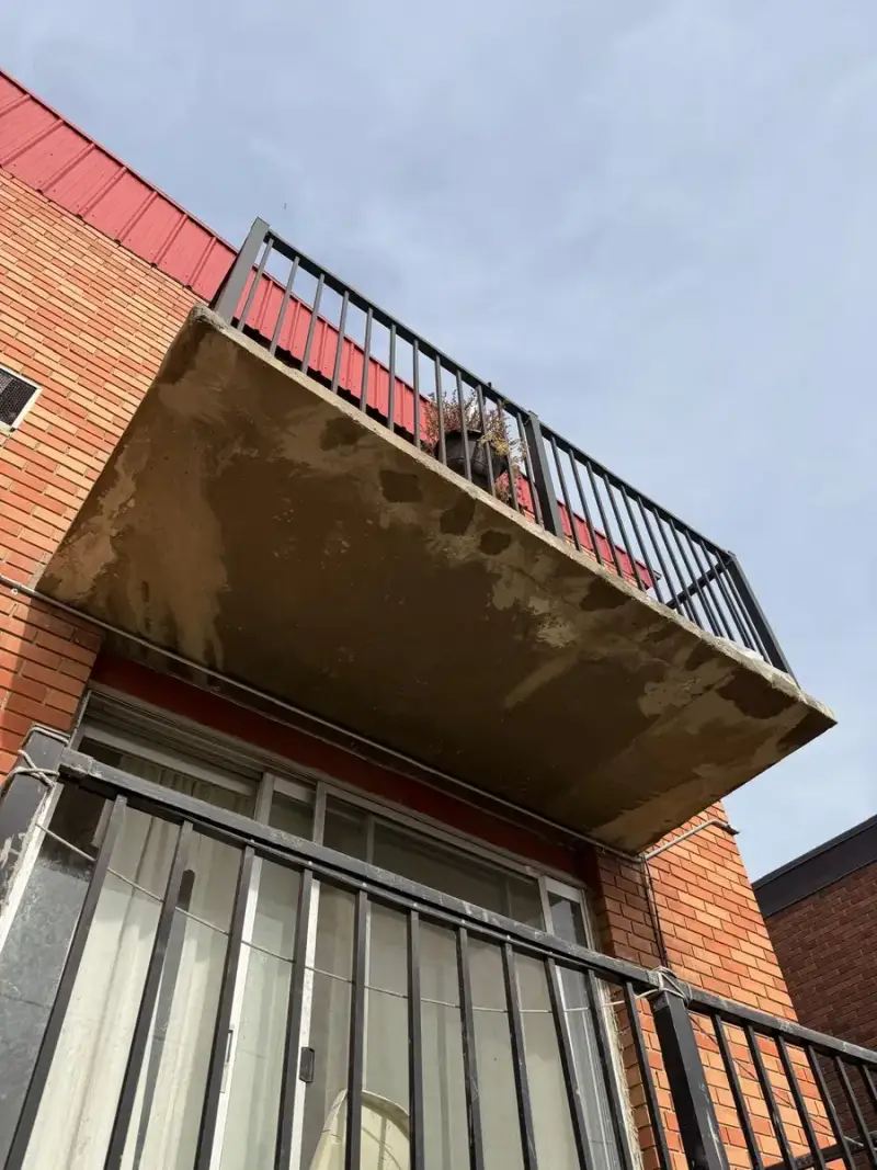 Underside of a concrete balcony slab with spalling and exposed rebar on an apartment building