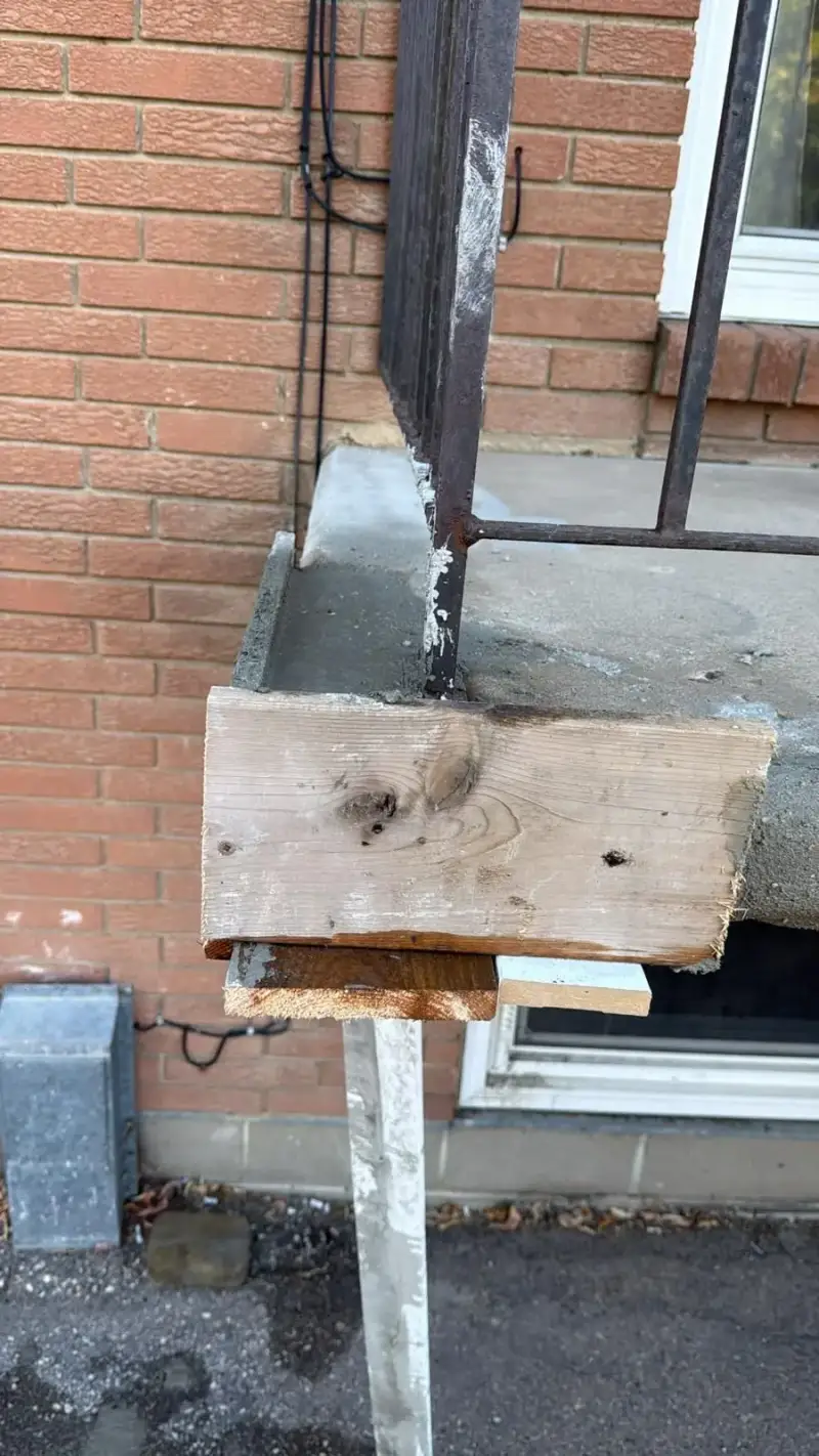 Concrete landing formed and poured with the railing post reset in fresh concrete beside a red brick wall