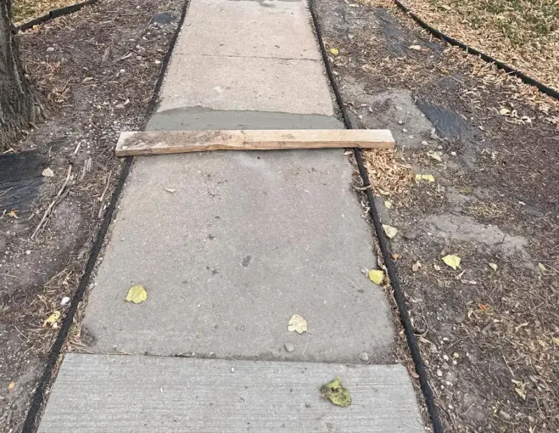 Concrete walkway with a form board laid across the new pour to keep foot traffic off