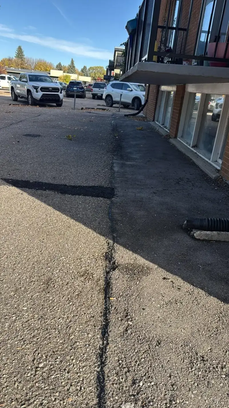 Crack seal running the length of the parking lot beside a red brick apartment building with balconies